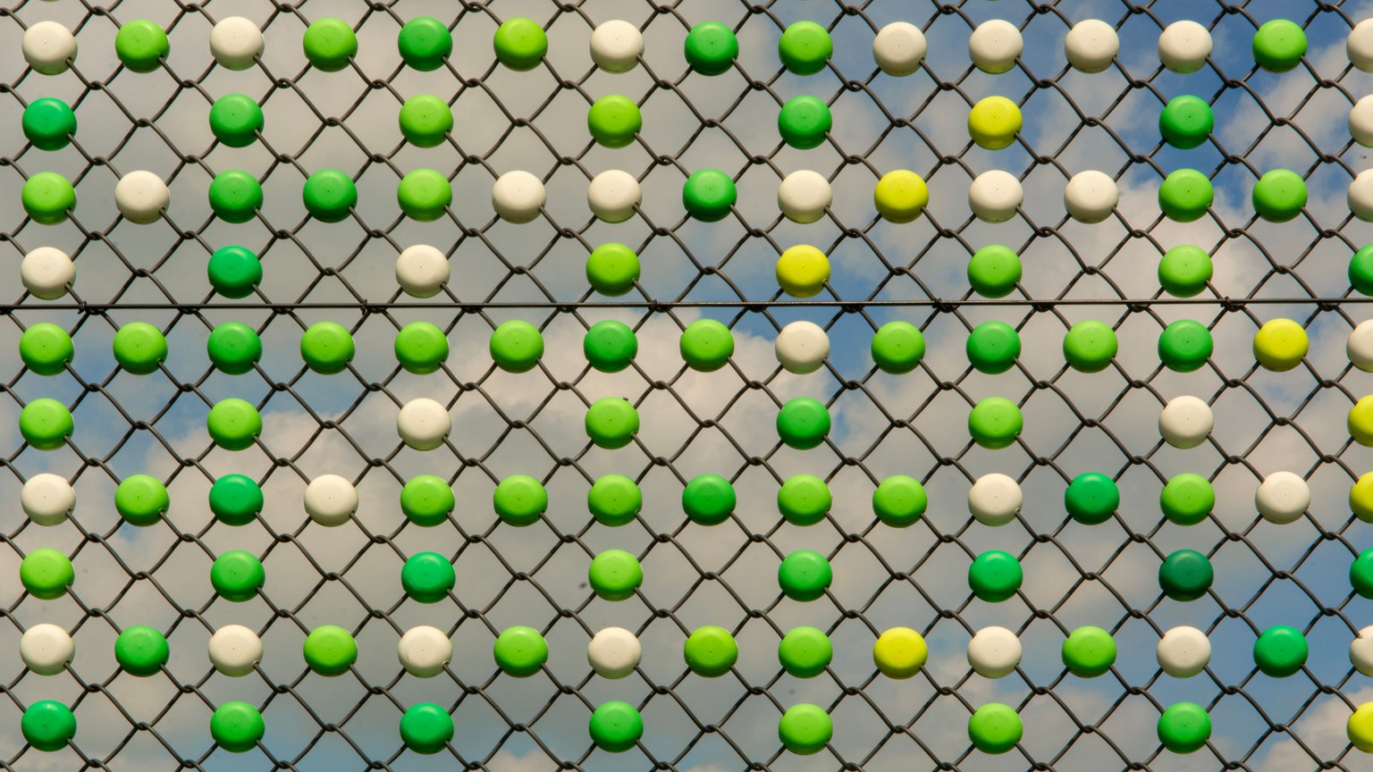 Bright geometric pattern on a fence with green and white circles against a blue sky.