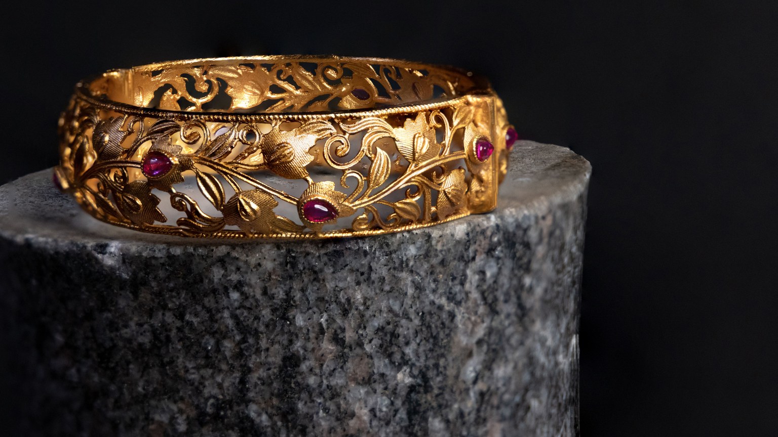 Intricate gold bracelet with ruby accents on a dark background. Luxurious and elegant design.