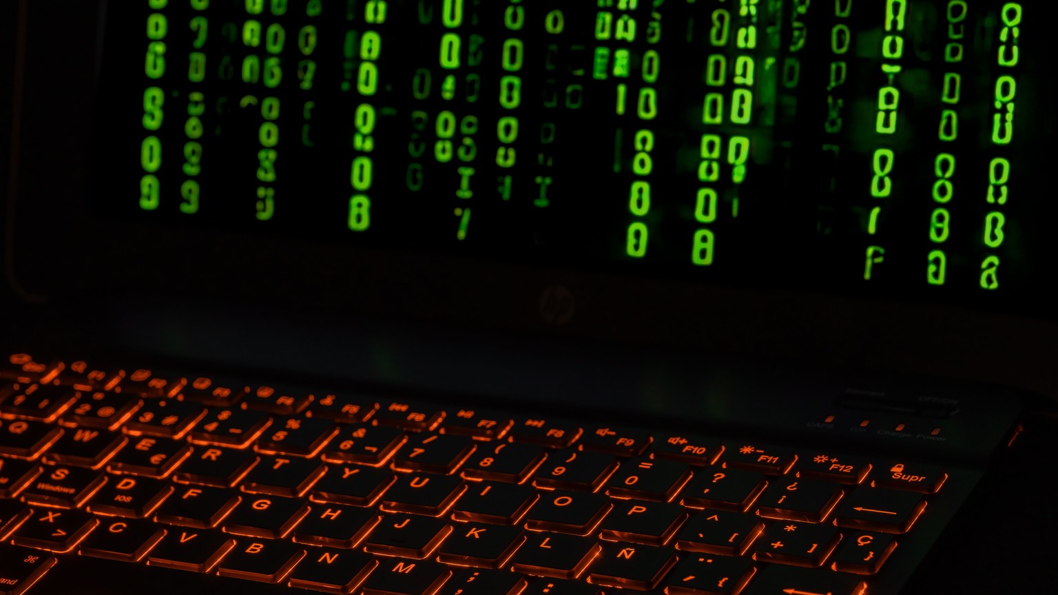 A laptop keyboard with orange backlight displaying green digital code symbols.