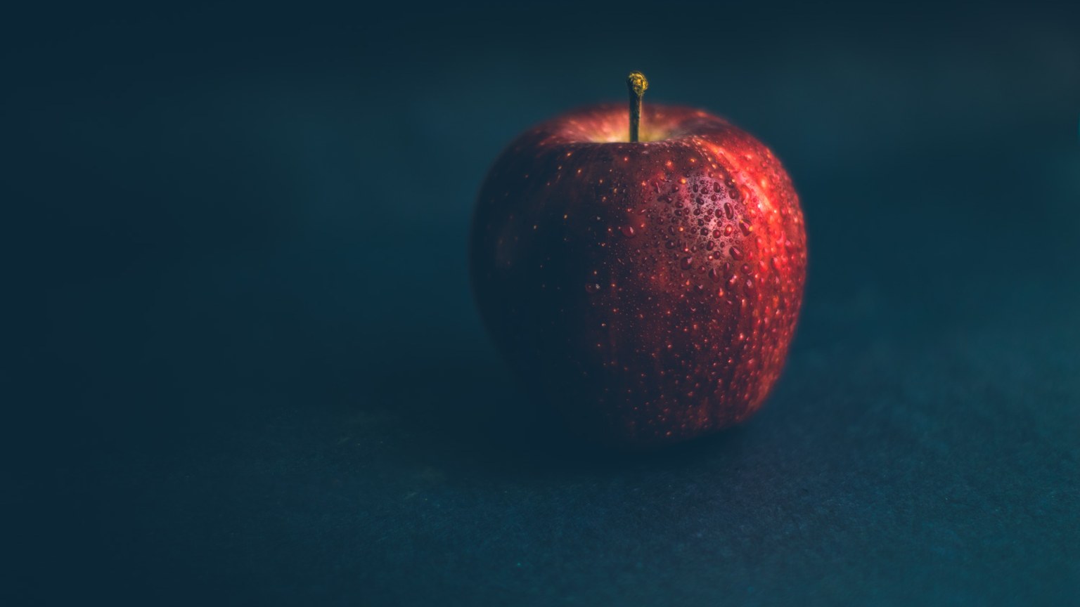 A vibrant red apple with glistening water droplets on a dark backdrop, emphasizing freshness and natural appeal.