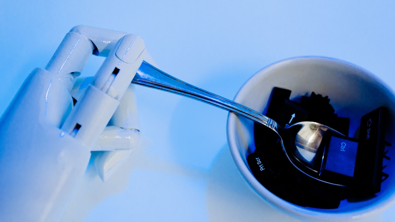 A robotic hand holding a spoon above a bowl with keyboard keys, showcasing technology themes.
