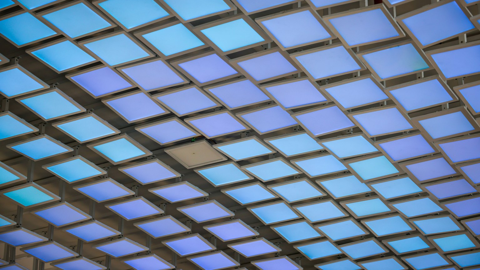 A modern ceiling installation featuring a grid of illuminated blue panels creating an abstract geometric pattern.
