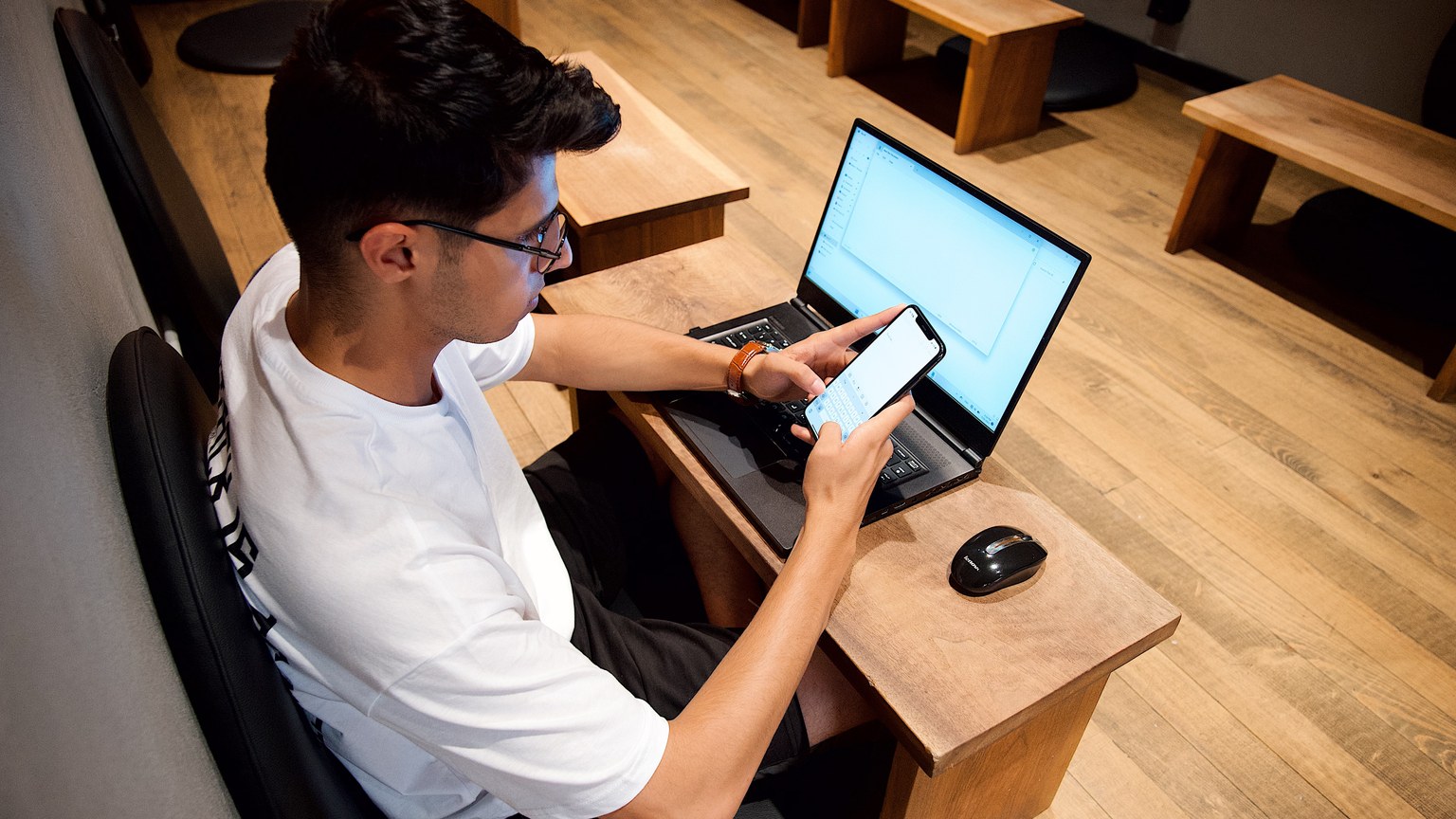 Man multitasking with a laptop and smartphone in a tech-friendly workspace.