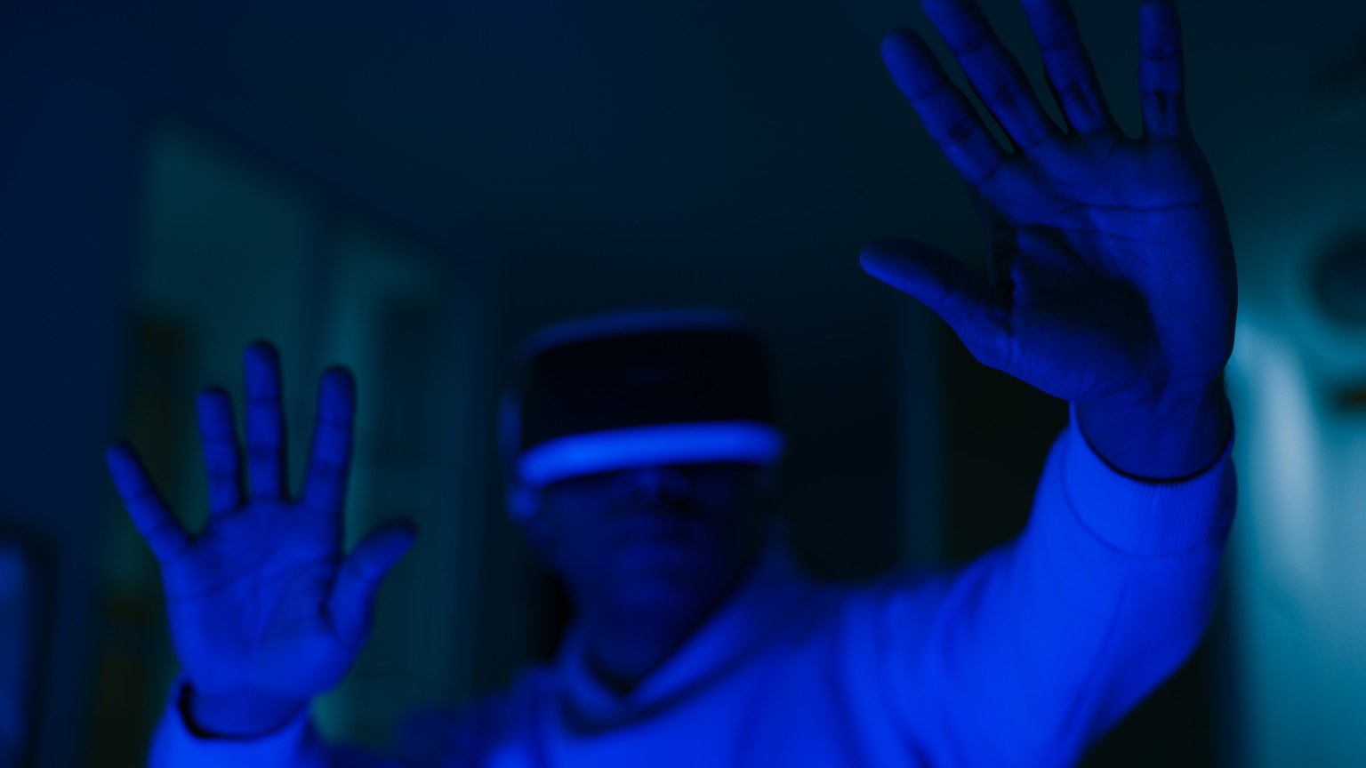 Man wearing VR headset immersed in virtual reality with visible hands in blue lighting.