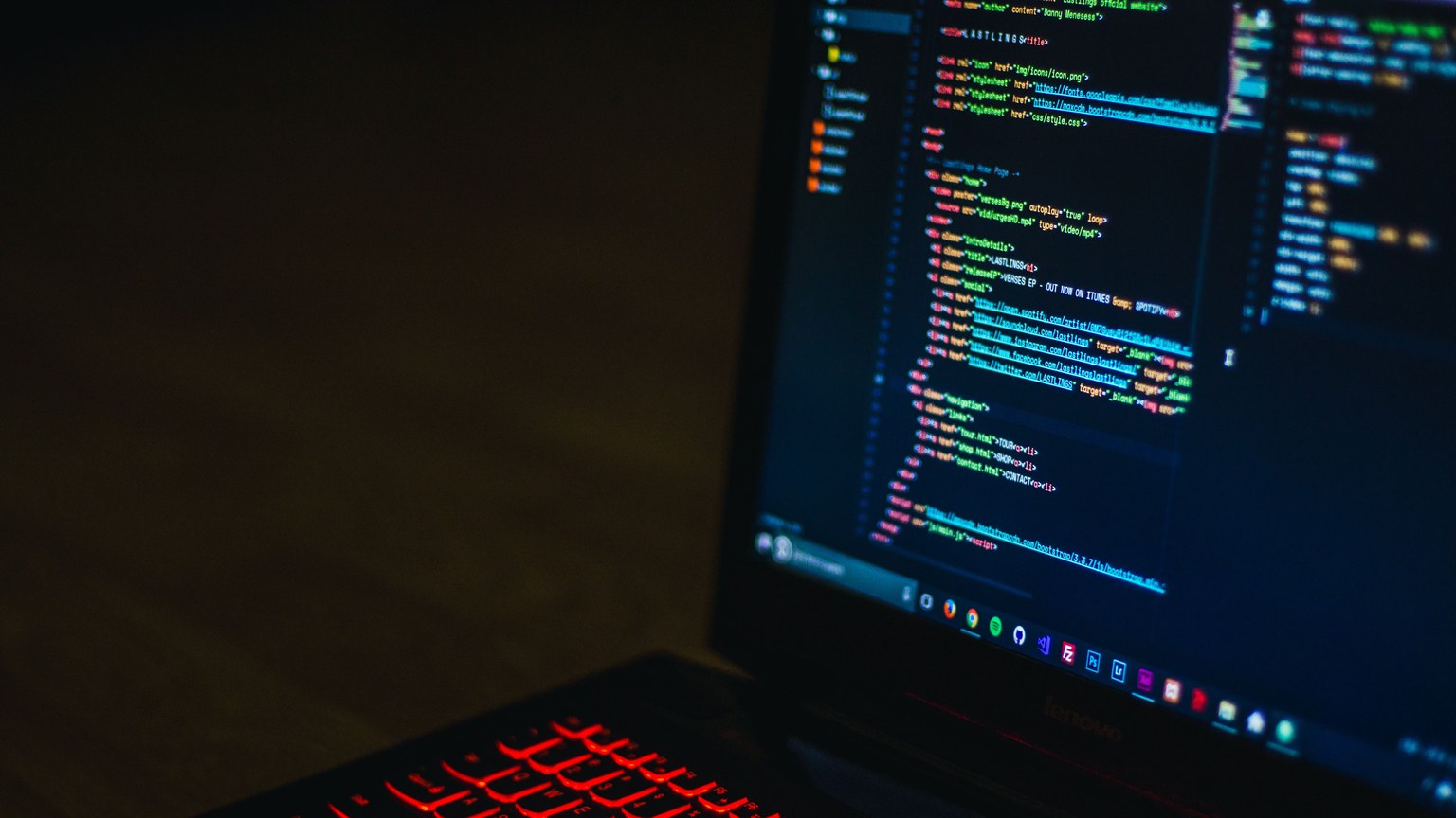 Red backlit keyboard and code on laptop screen create a tech-focused ambiance.