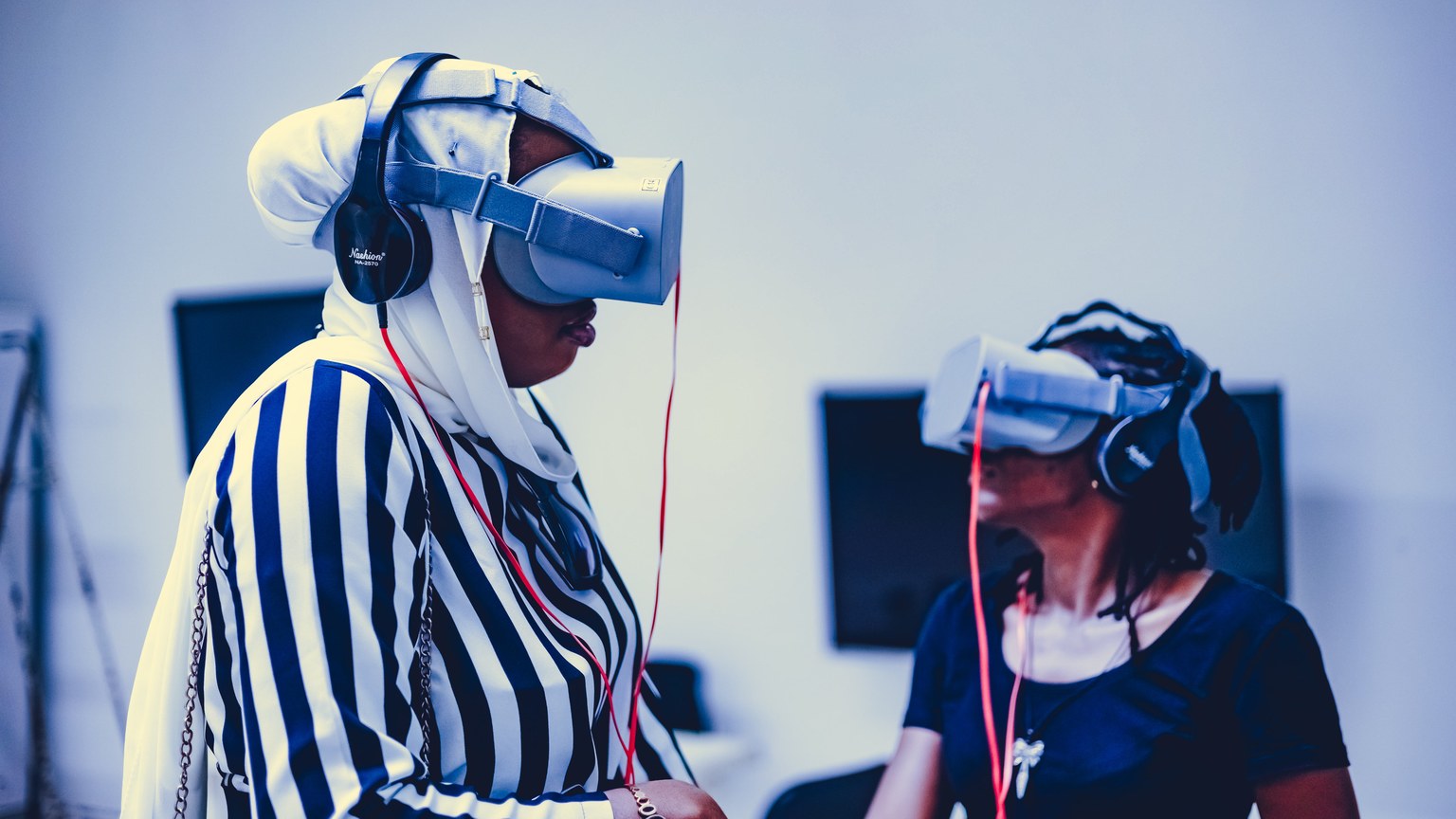 Two women using virtual reality headsets indoors, exploring immersive technology.