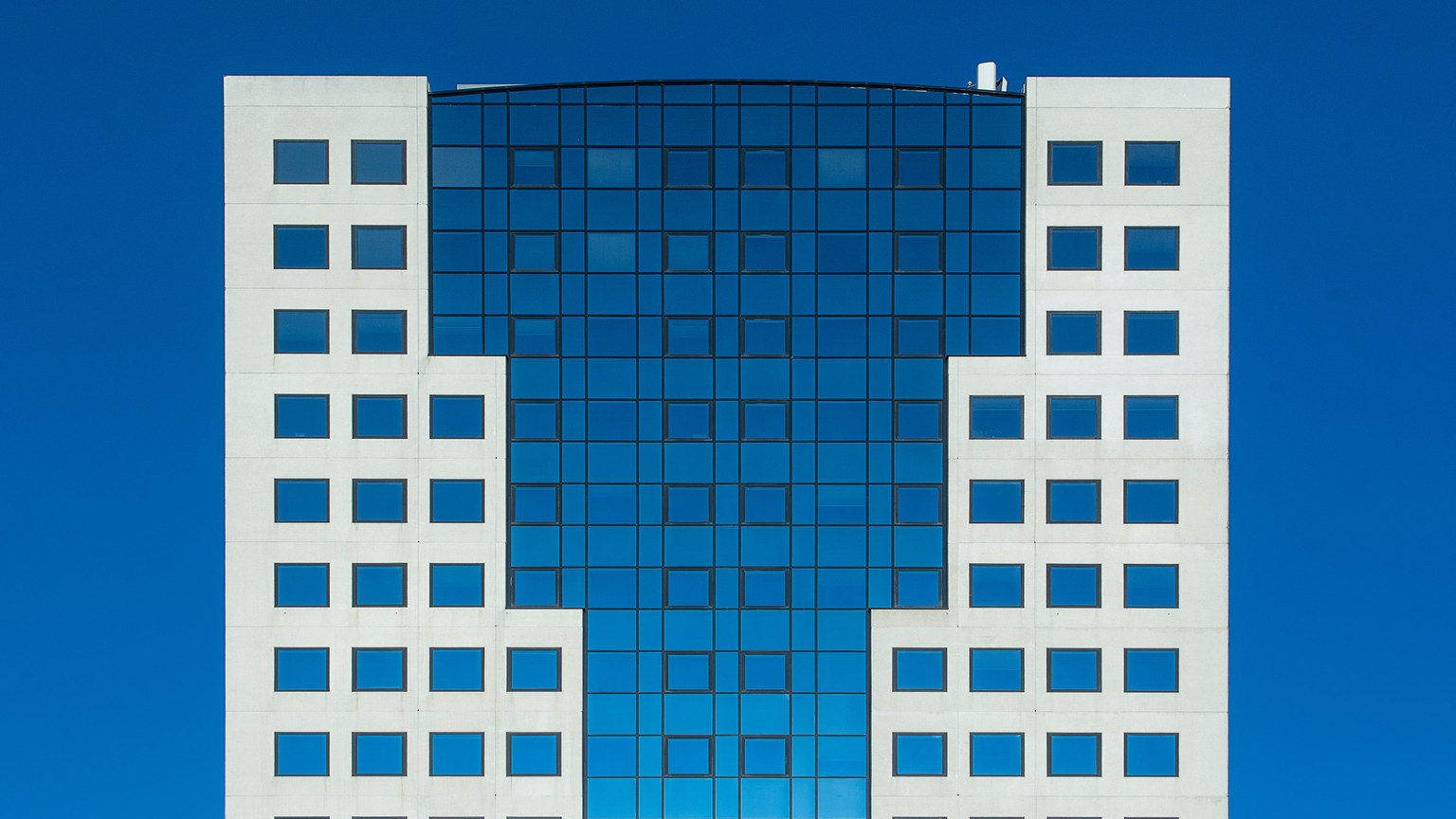 A modern office building featuring a striking geometric facade against a clear blue sky.