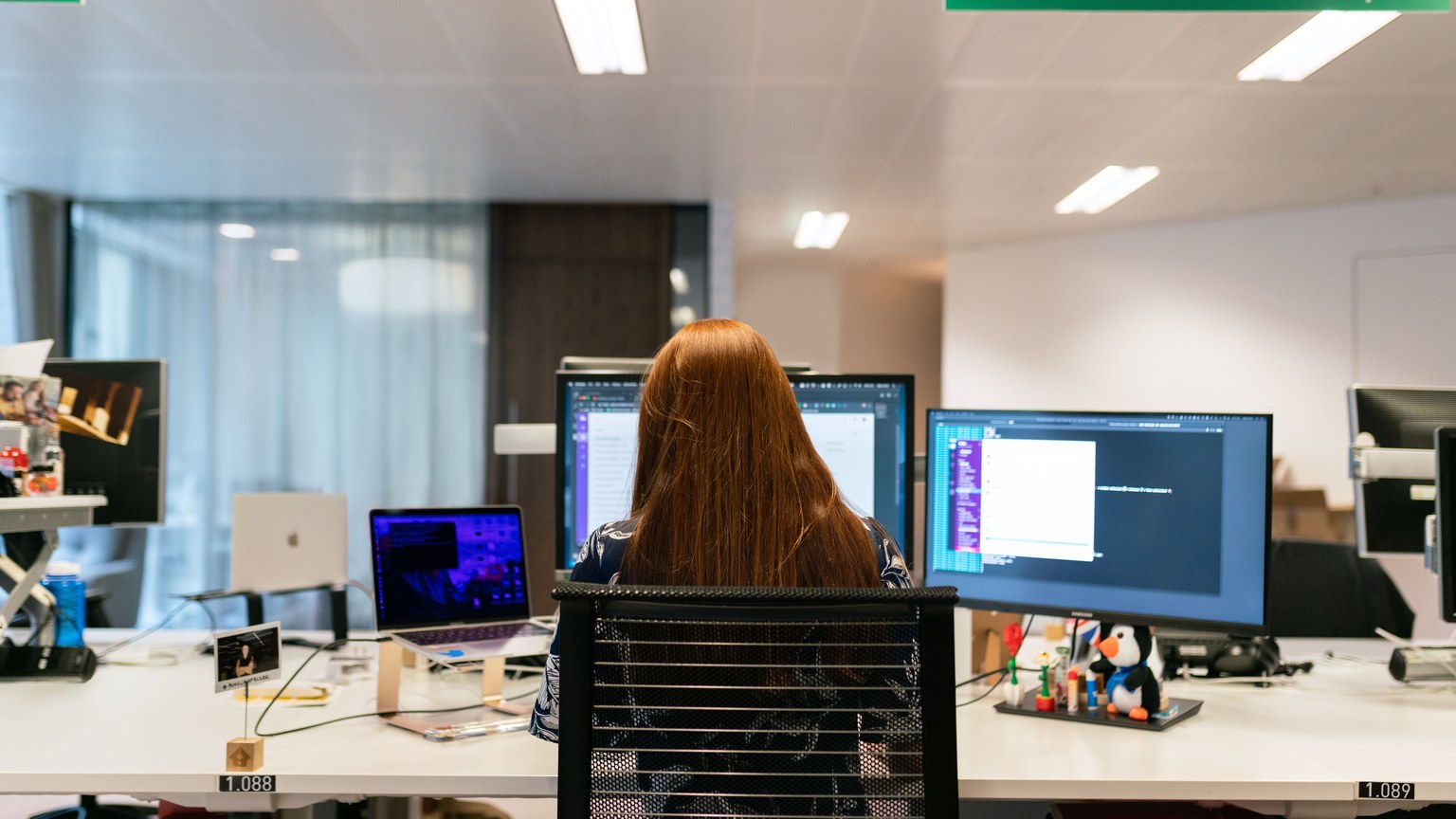 Back view of a female software engineer working at a multi-monitor setup in an office.