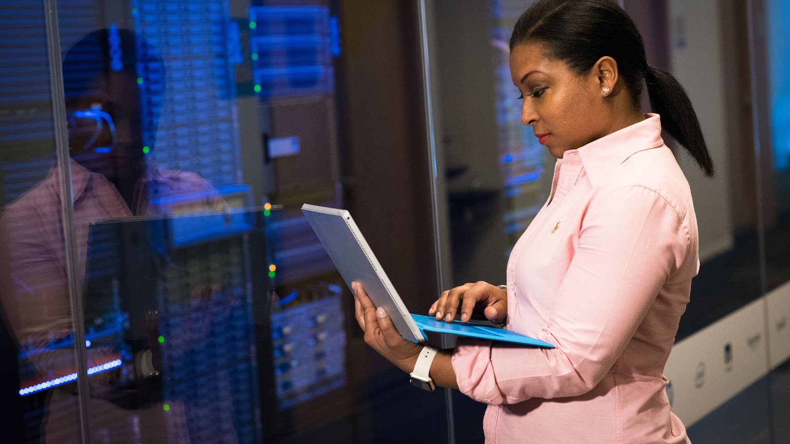 A focused software engineer working on a laptop in a server room, reflecting dedication in tech.