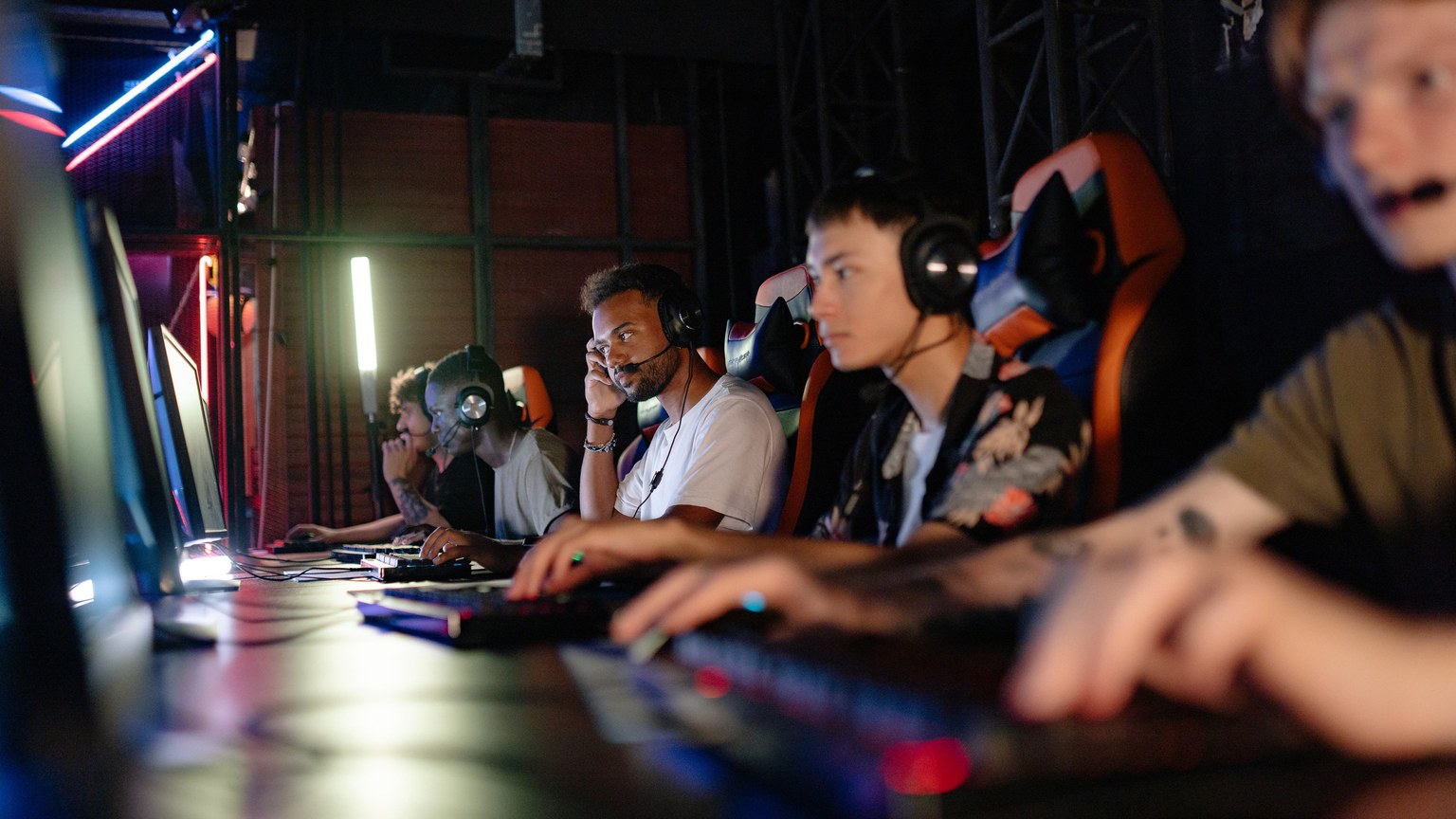 A group of young adults engaged in a focused PC gaming session indoors.