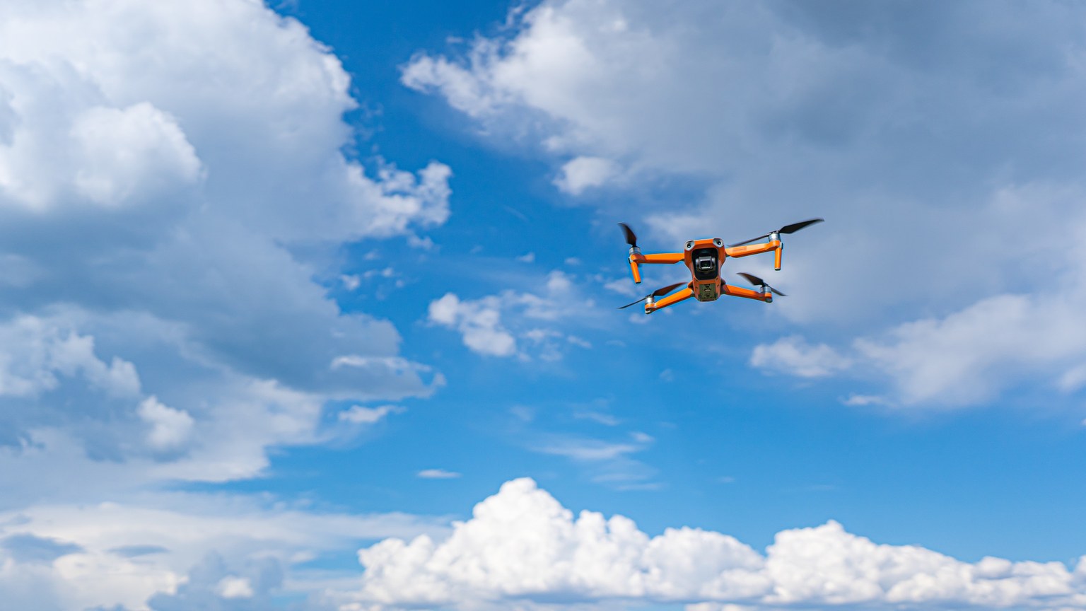 Drone flying mid-air against a vibrant blue sky with fluffy clouds, showcasing modern technology and aerial photography.