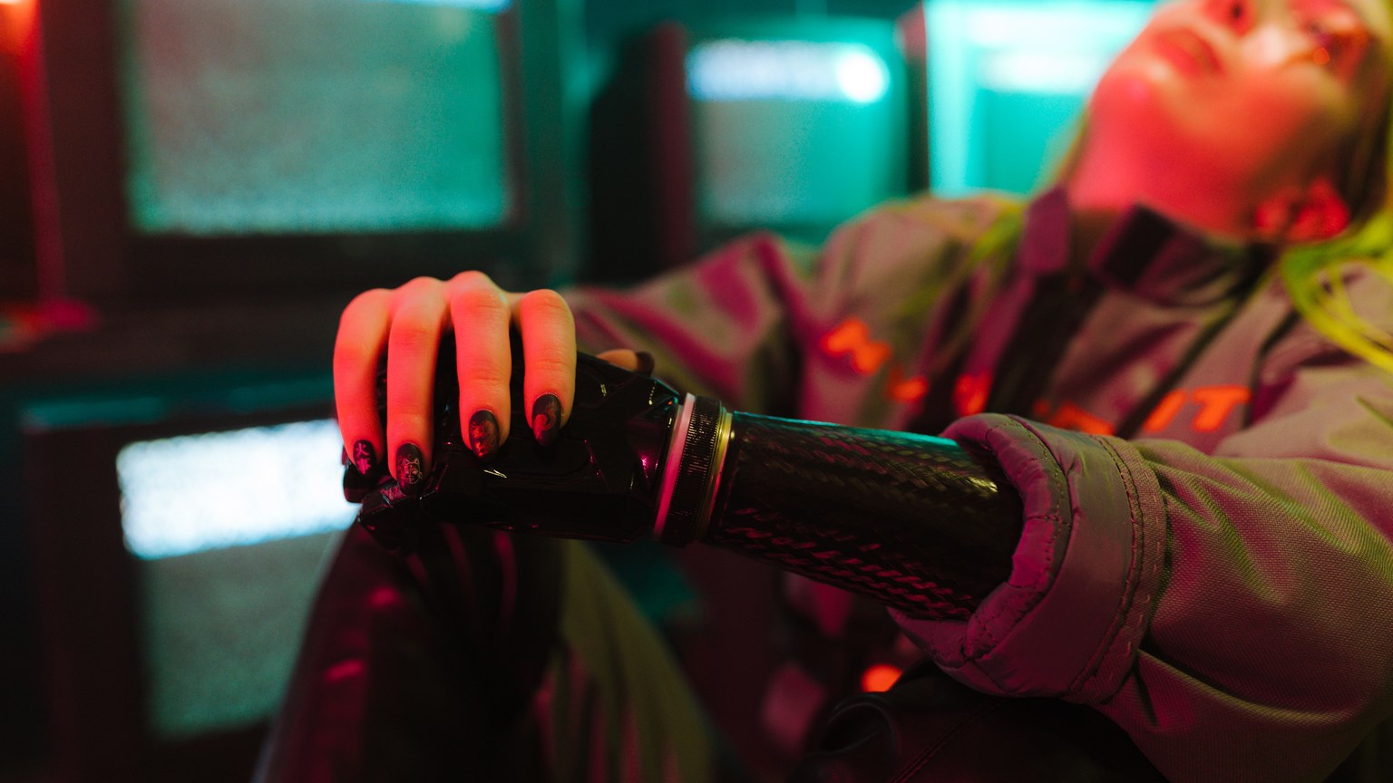 Close-up of a person with a prosthetic arm in a cyberpunk setting.