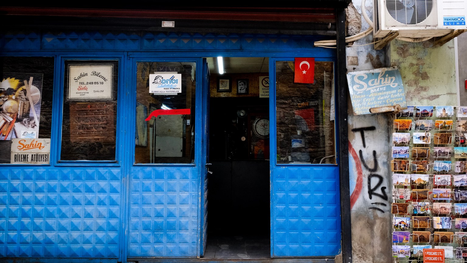 A rustic blue storefront adorned with a Turkish flag and a display of postcards.