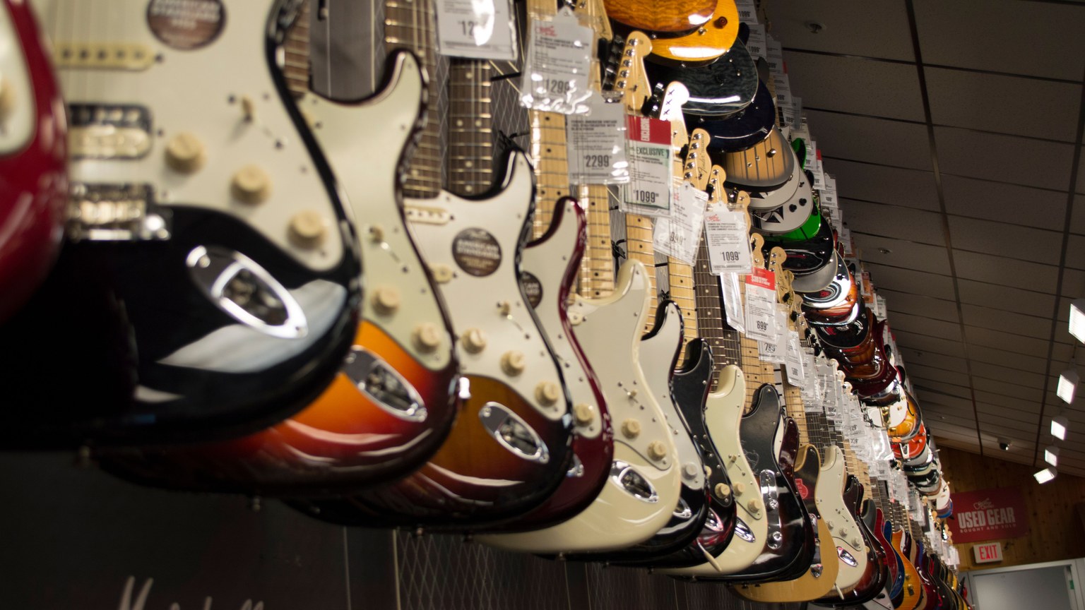 Row of colorful electric guitars hanging in a music store, showcasing diverse models and prices.