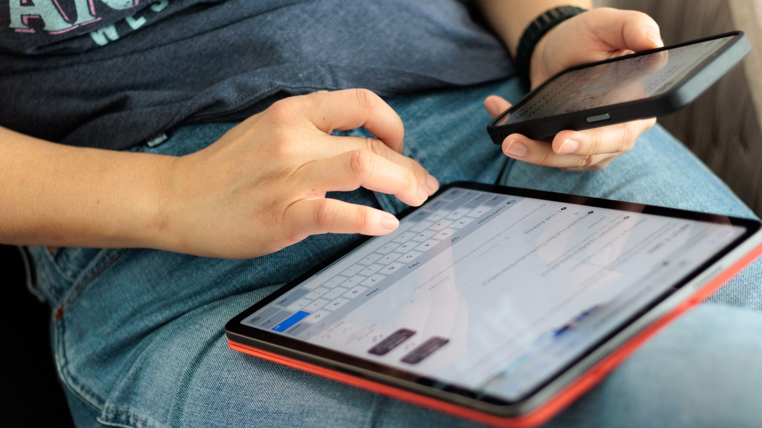 Close-up of adult using a tablet and smartphone indoors, showcasing digital connectivity and multitasking.