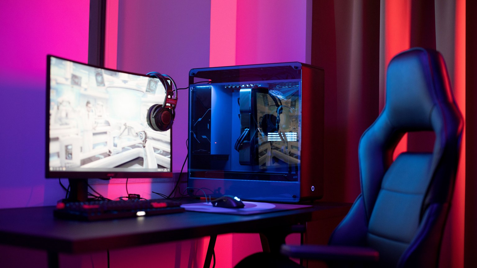A sleek gaming setup featuring a high-end PC, widescreen monitor, and ergonomic chair lit by neon lights.