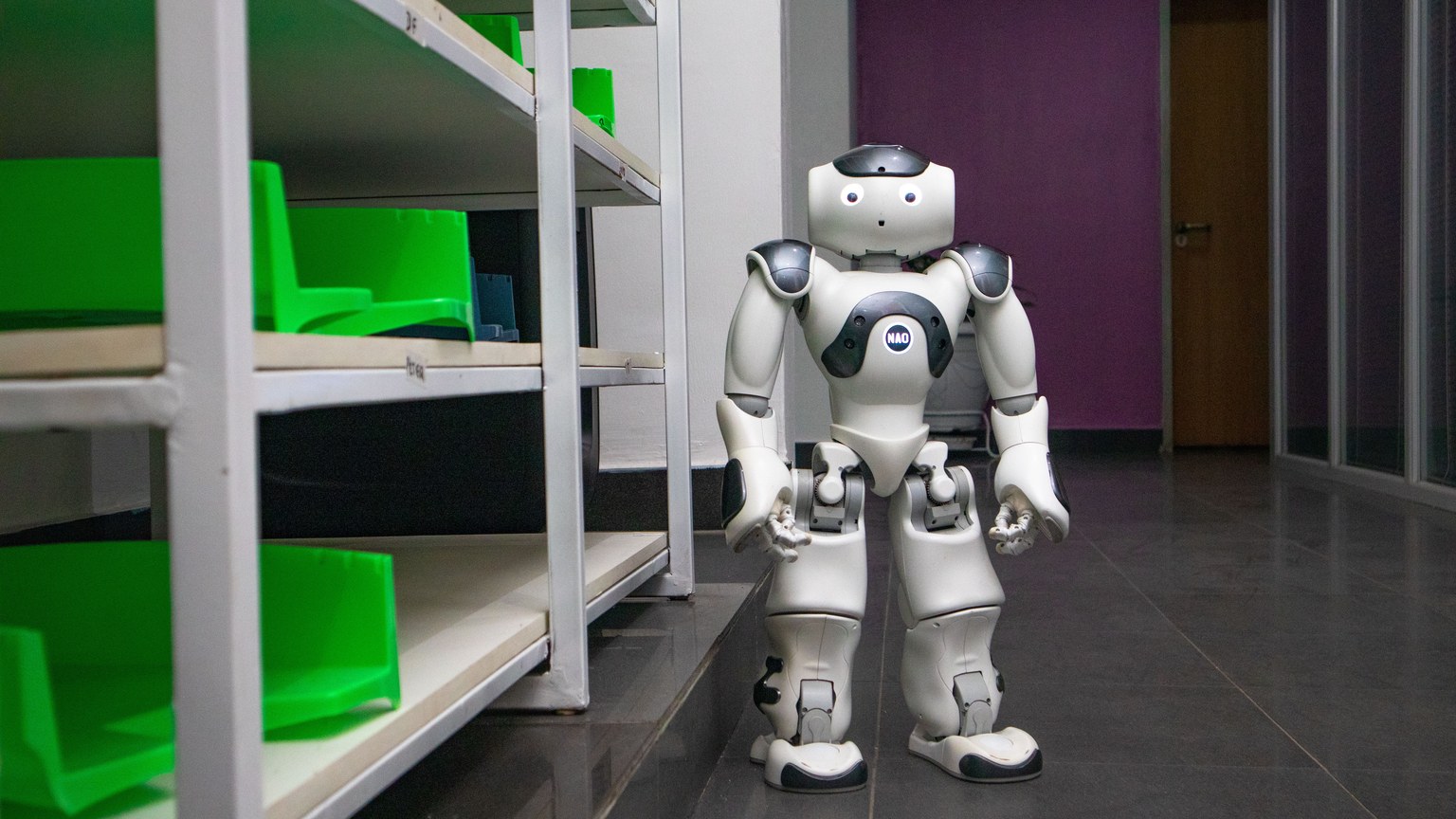 A humanoid robot standing in a modern corridor with shelves, representing futuristic technology.