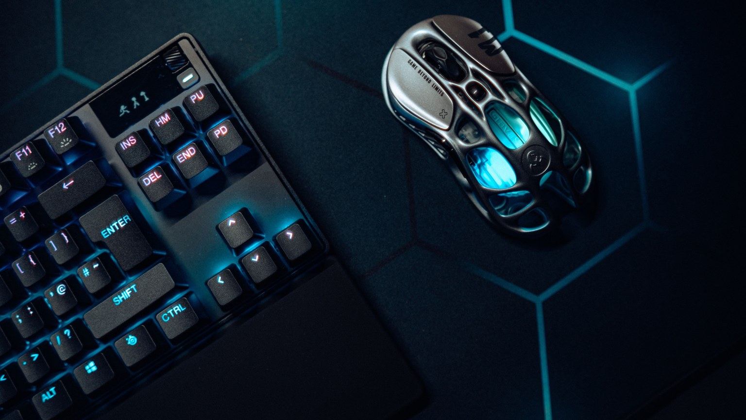 Futuristic gaming mouse and mechanical keyboard with blue LED lighting on hexagonal backdrop.