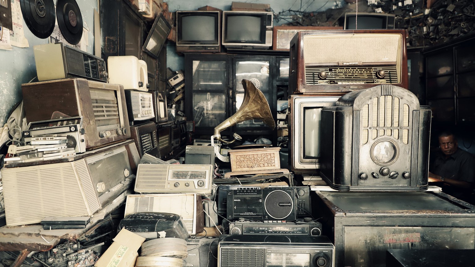 An array of vintage electronics, radios, and a gramophone in an antique shop with a nostalgic atmosphere.