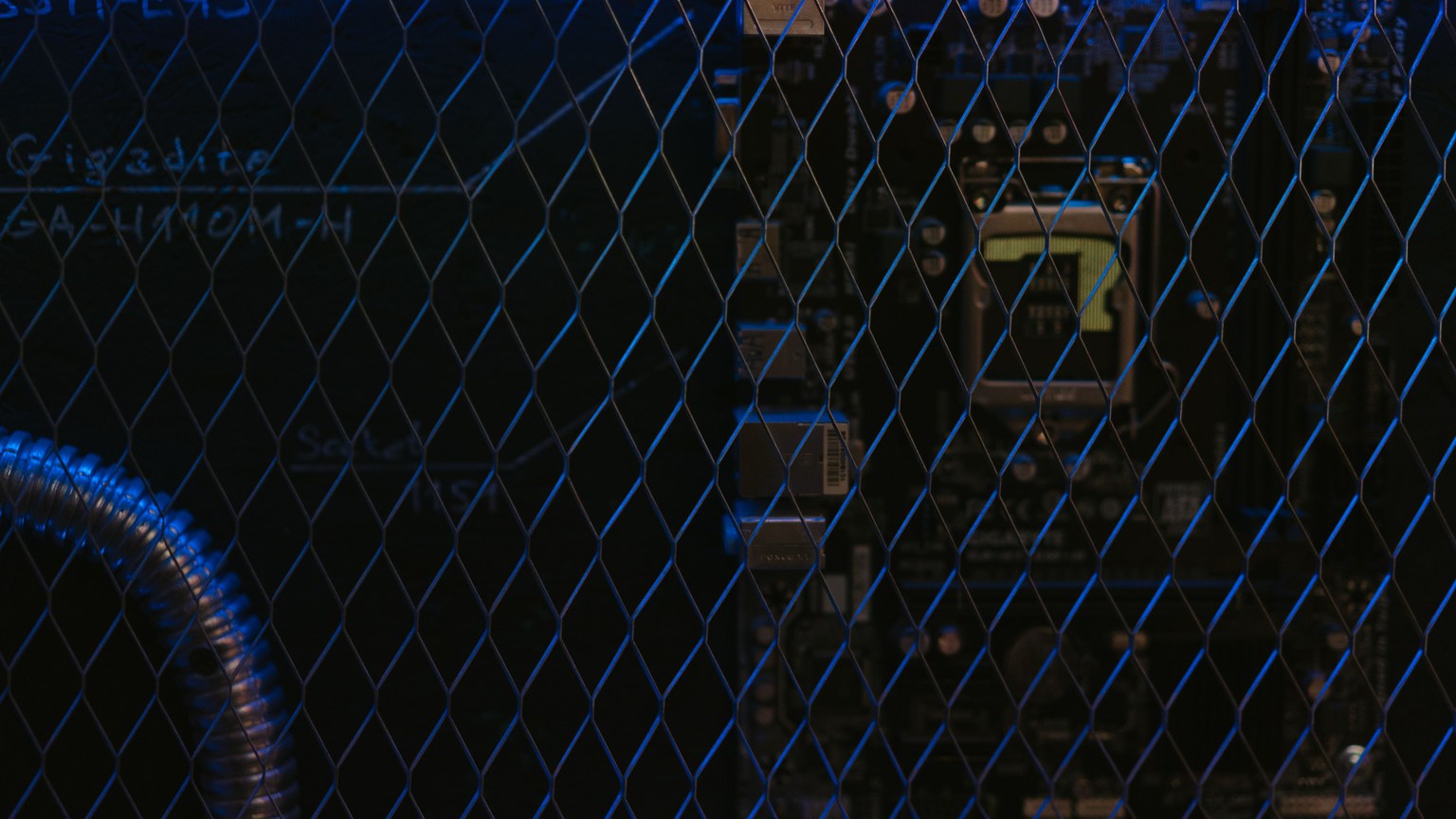 Artistic view of a circuit board through metal mesh with blue lighting.