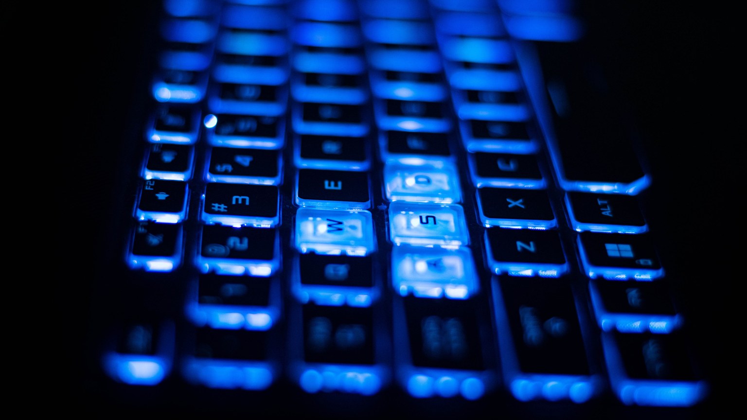 Close-up shot of a vibrant blue backlit keyboard keys on a laptop.