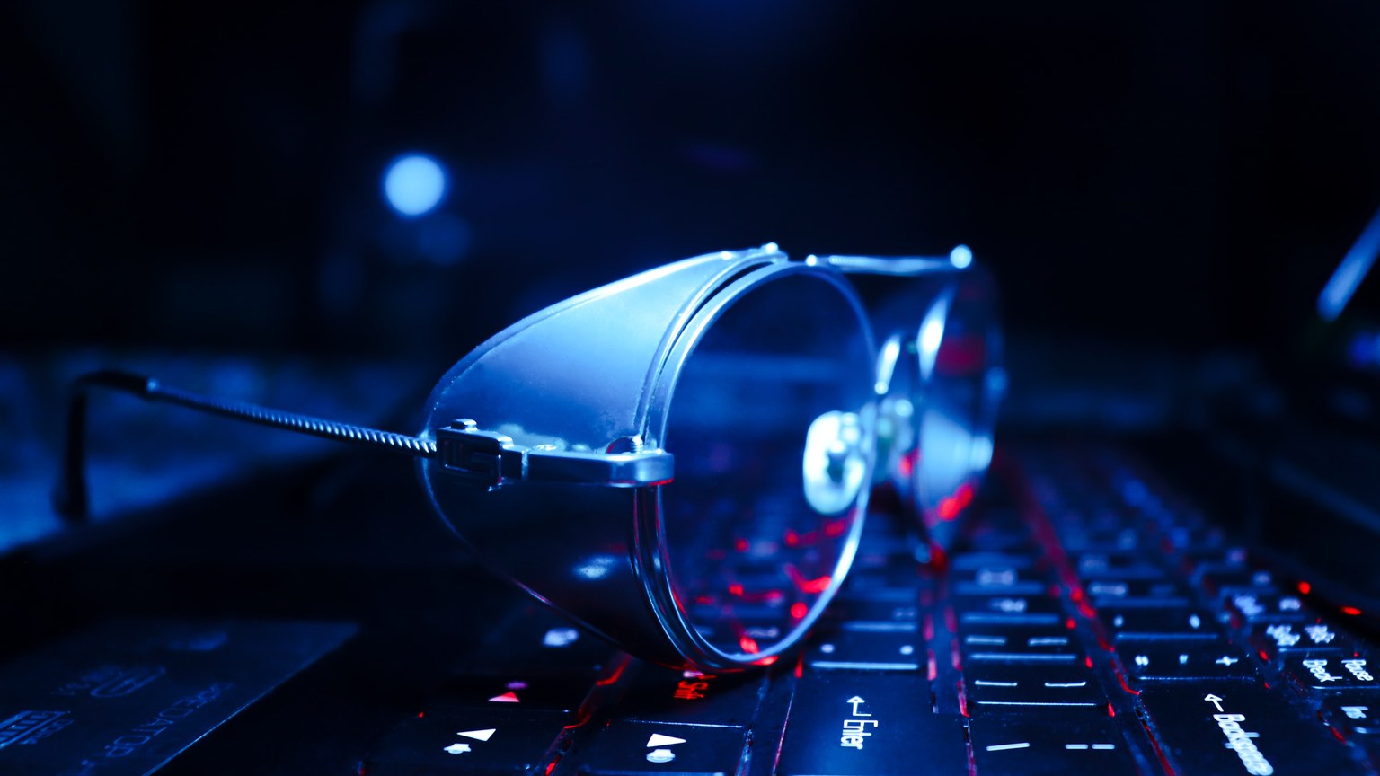 Close-up of eyeglasses on a glowing laptop keyboard, symbolizing technology and work.