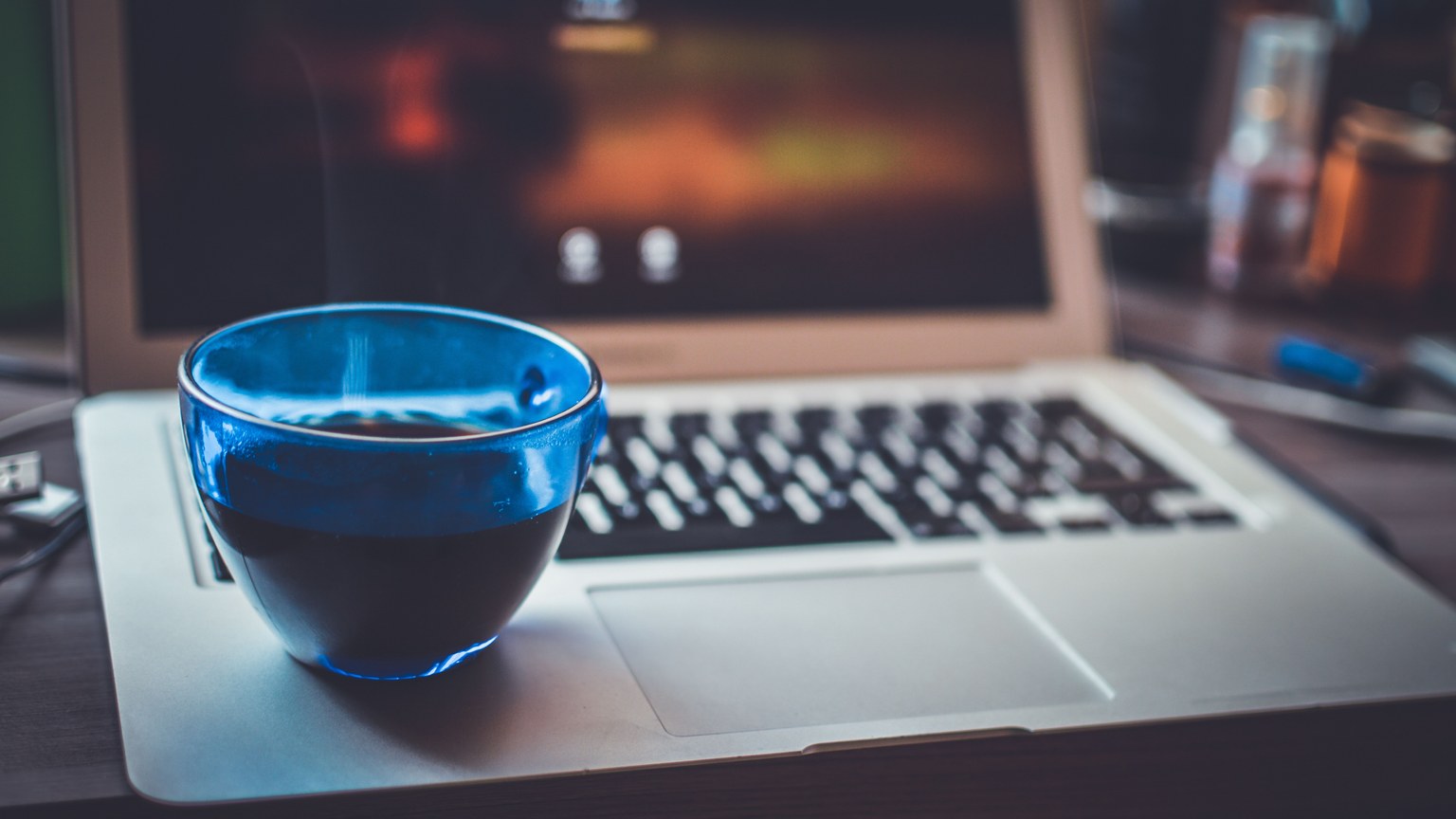 A blue glass cup with a warm beverage on an open laptop, blending technology and relaxation.