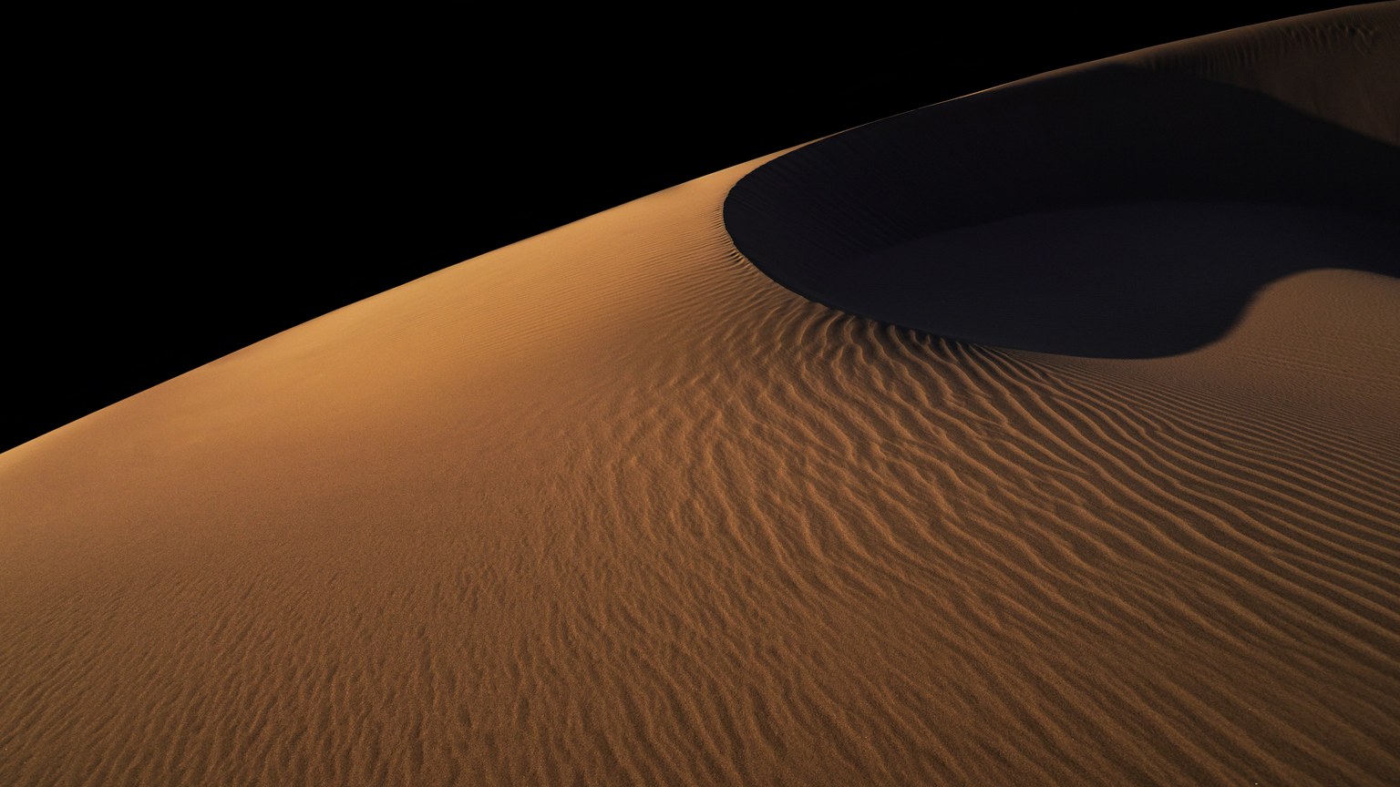 A dramatic view of a desert dune at night with deep shadows and ripples.
