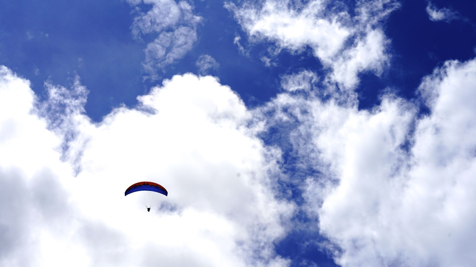 A paraglider soars through a bright blue sky filled with white clouds, capturing the essence of freedom and adventure.
