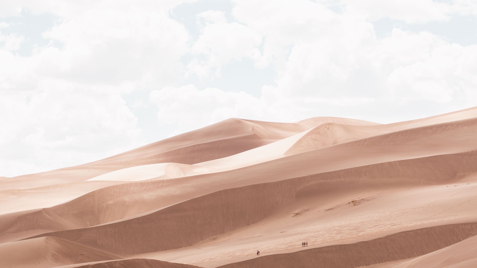 Expansive sand dunes stretch under a sky dotted with white clouds, capturing nature's untouched beauty.