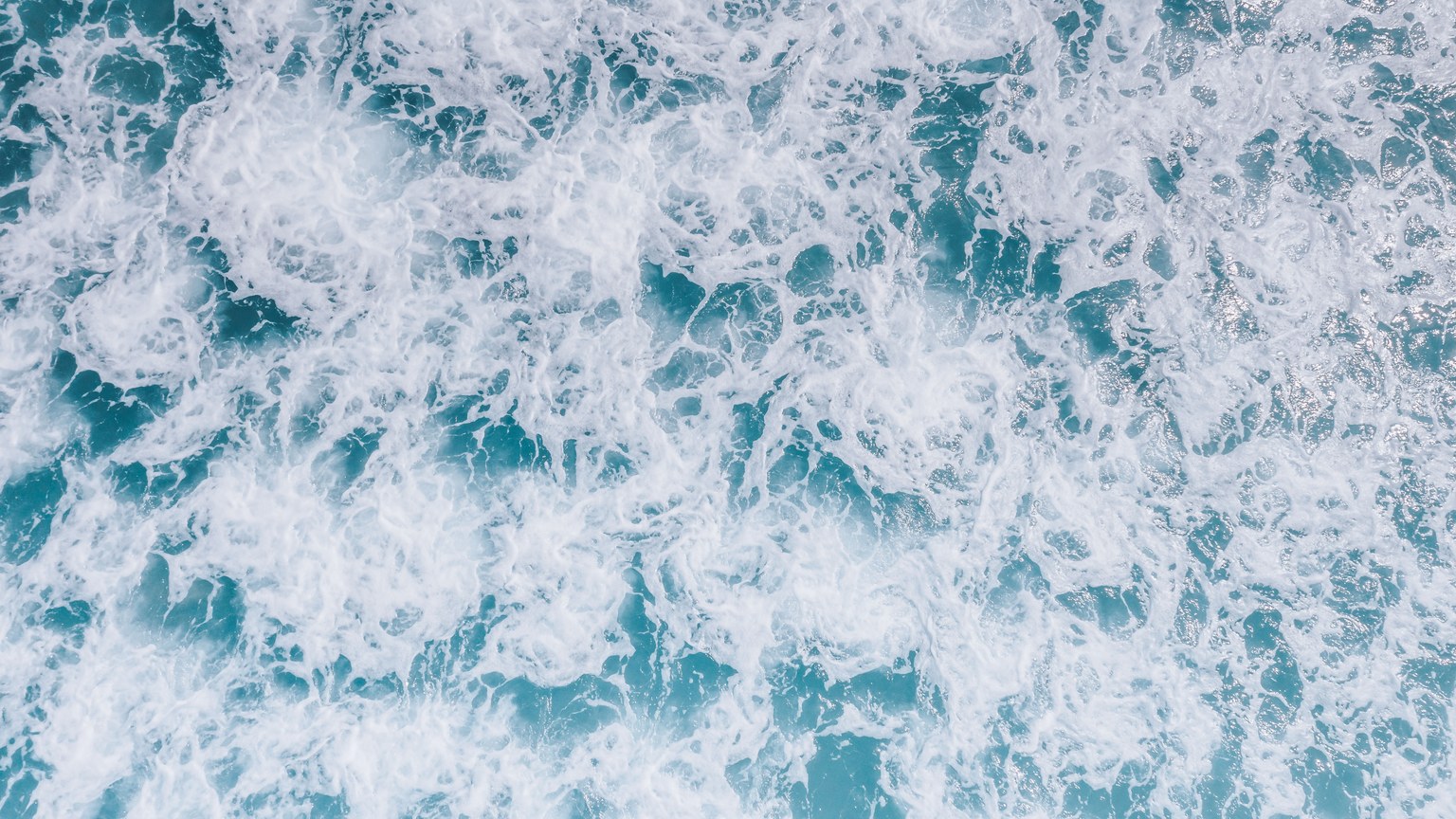 A dynamic top view of ocean waves and sea foam demonstrating nature's power and beauty.