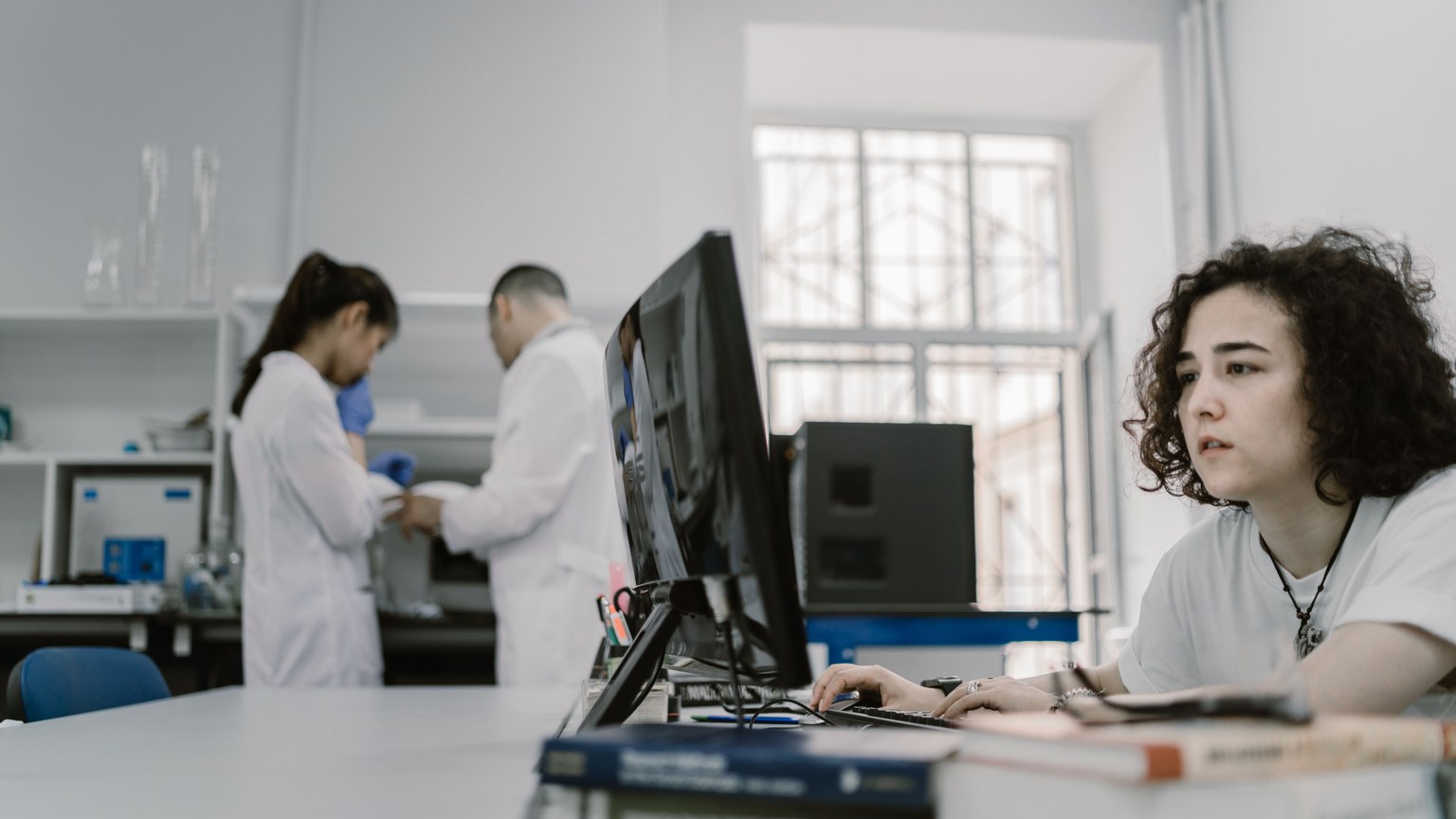 Focused woman working on a computer in a busy laboratory setting, showcasing teamwork and scientific research.