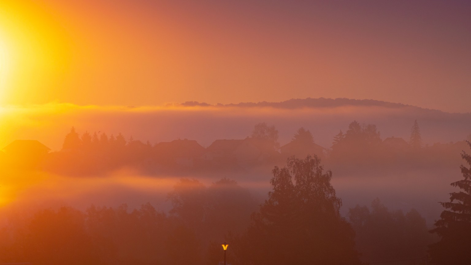 A captivating sunrise over a foggy landscape with vibrant warm colors and silhouettes.