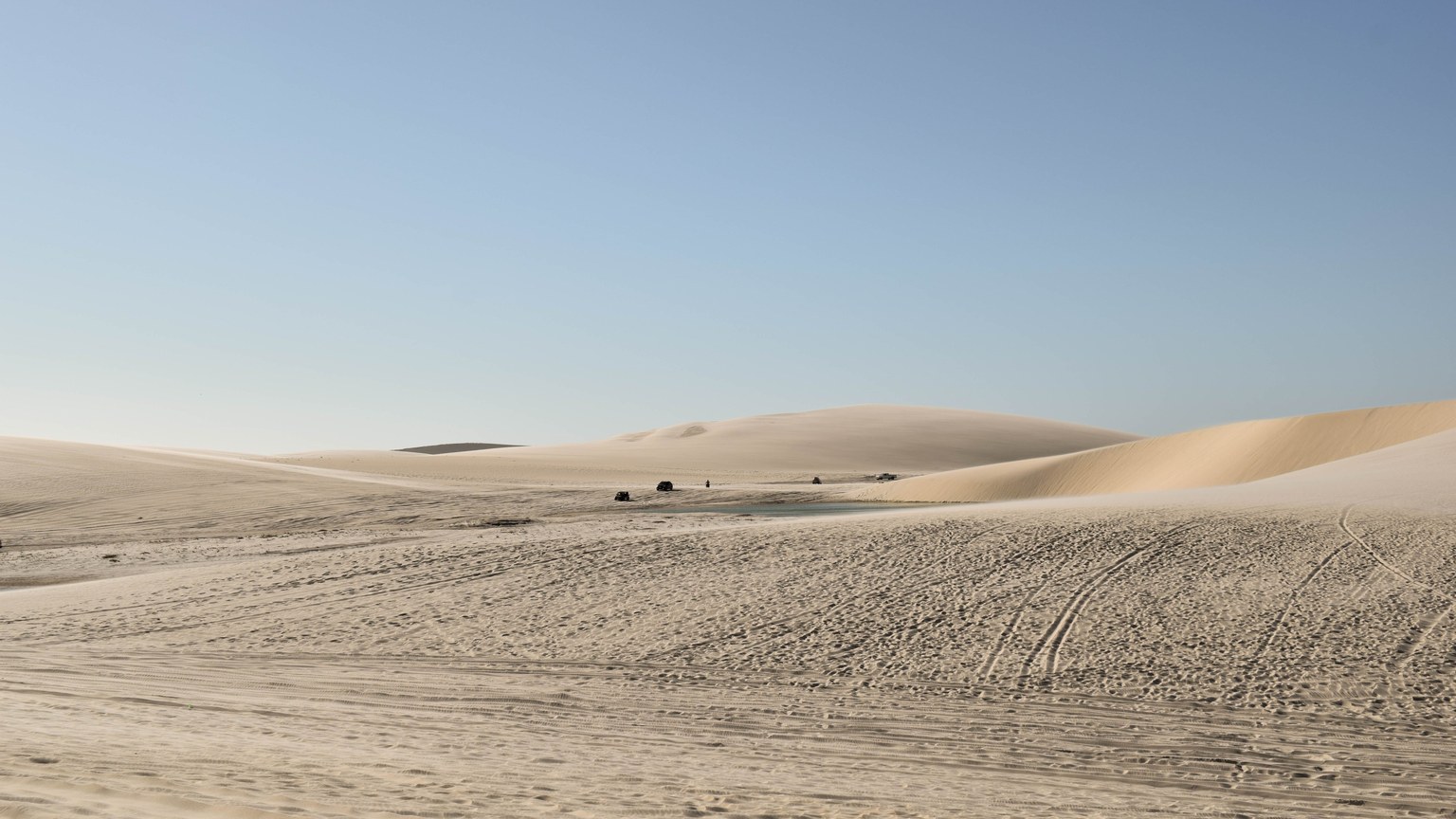 Vast desert with rolling sand dunes under a clear blue sky, epitomizing isolation and natural beauty.