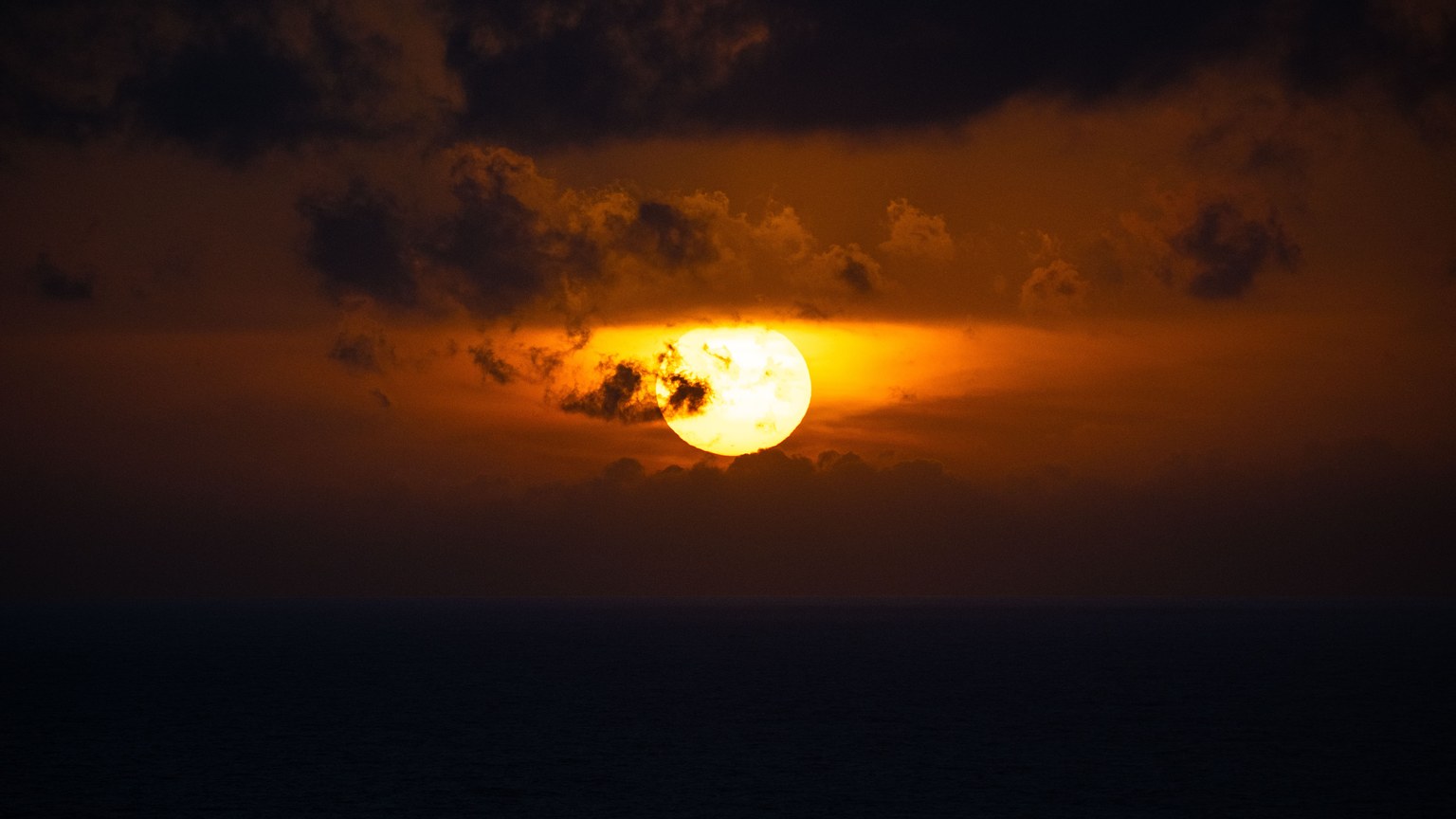 A breathtaking view of a fiery sunset over the ocean, casting a warm glow and dramatic clouds.