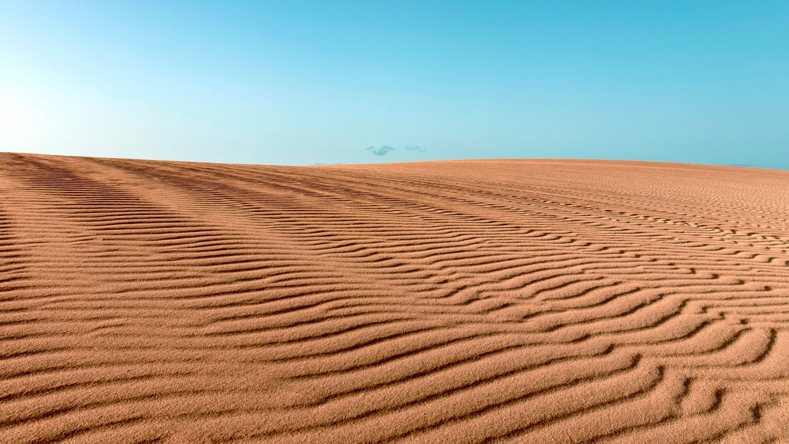 Stunning desert landscape with rippled sand dunes under a vibrant blue sky in Spain.