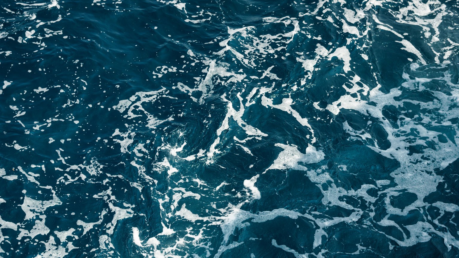 A mesmerizing view of the deep blue ocean with intricate white foam patterns captured from above.
