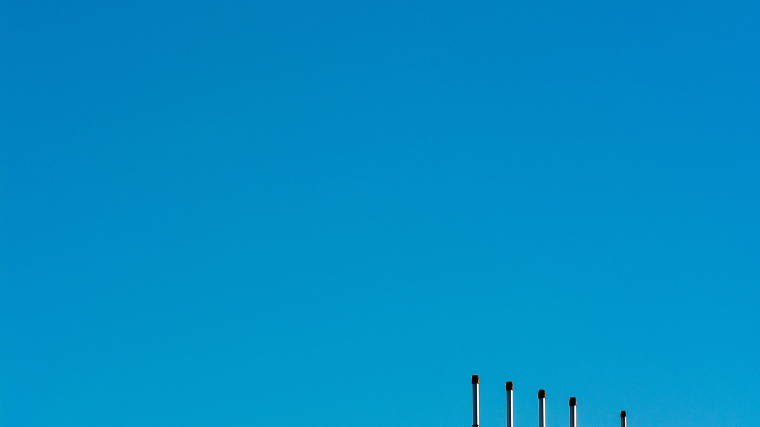 Minimalist image of industrial poles under a clear blue sky, highlighting clean energy.