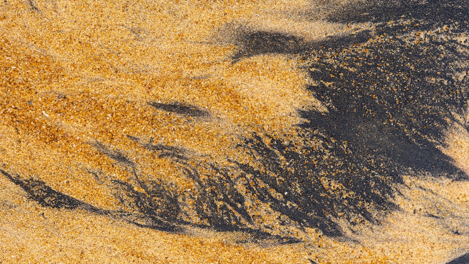 Close-up of ilmenite and yellow sand forming natural abstract patterns on a beach.