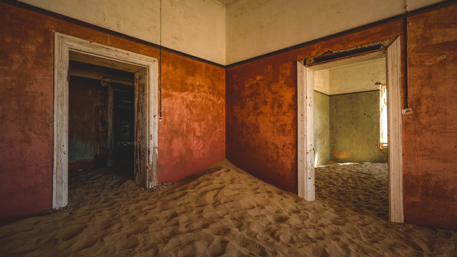 Eerie abandoned house in Kolmanskop, Namibia, with sand-filled interiors, showcasing decay and desert encroachment.