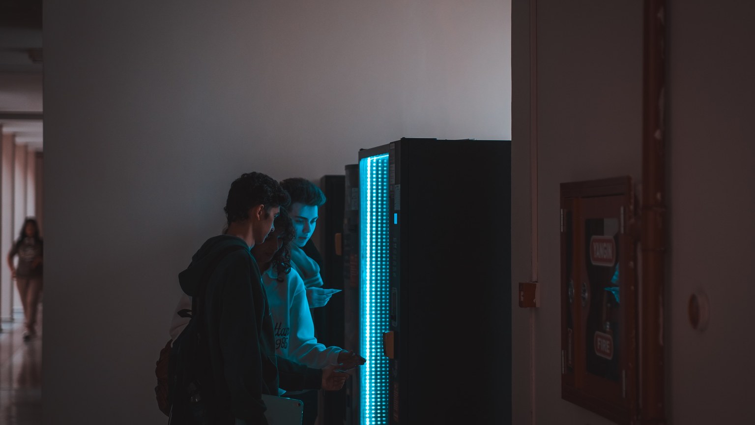 Group of teenagers using a vending machine in a school corridor, captured in ambient lighting.