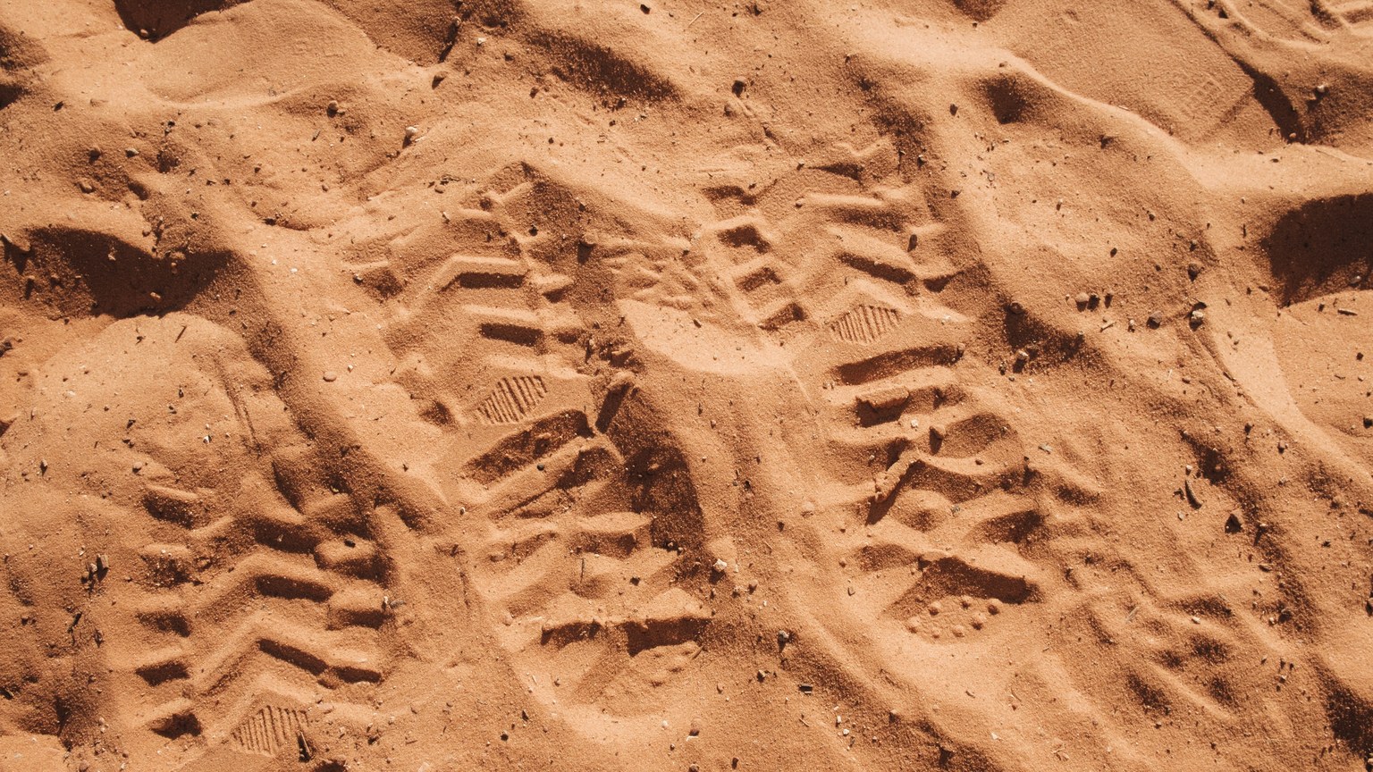 Detailed footprints on desert sand, showing shoe tread patterns in a warm setting.