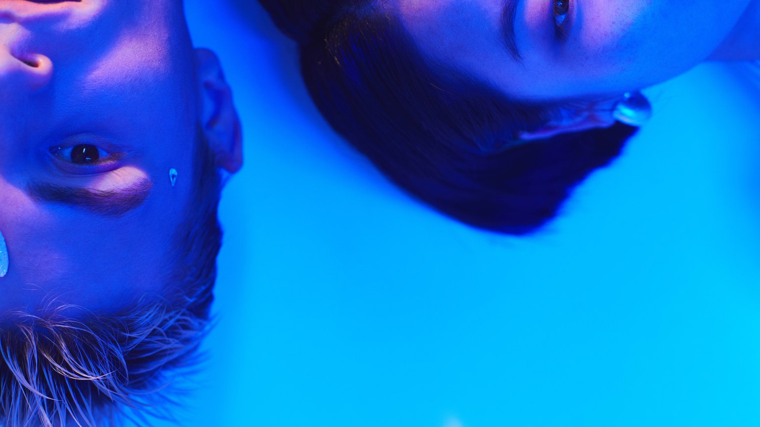 Close-up of two young individuals in a futuristic blue light setting.