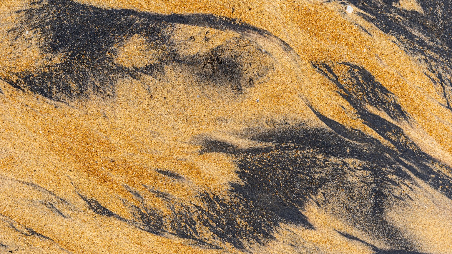 Close-up of black and yellow sand patterns on a beach showcasing natural textures.