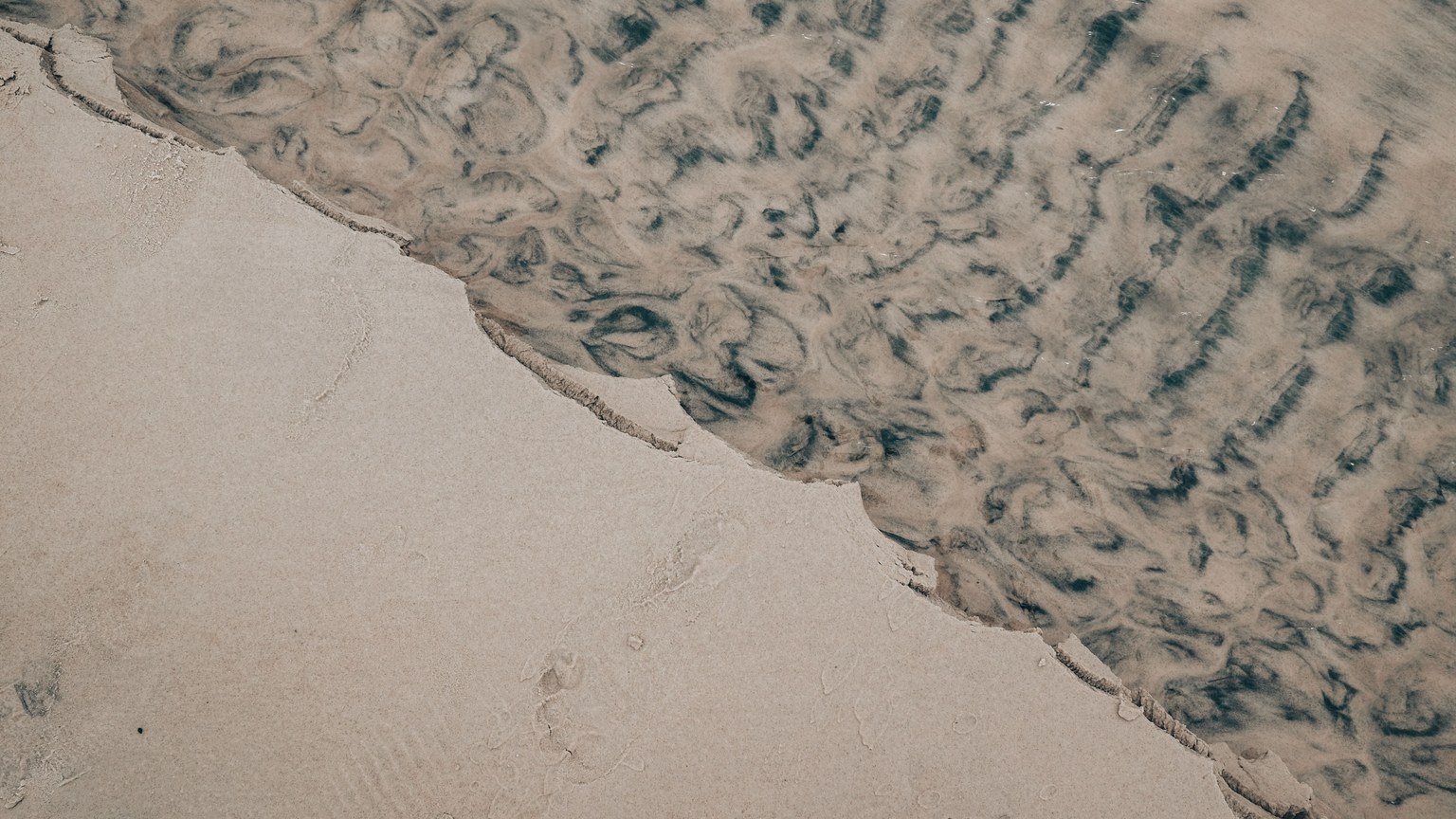 Abstract patterns of sand and water on a serene beach shore.