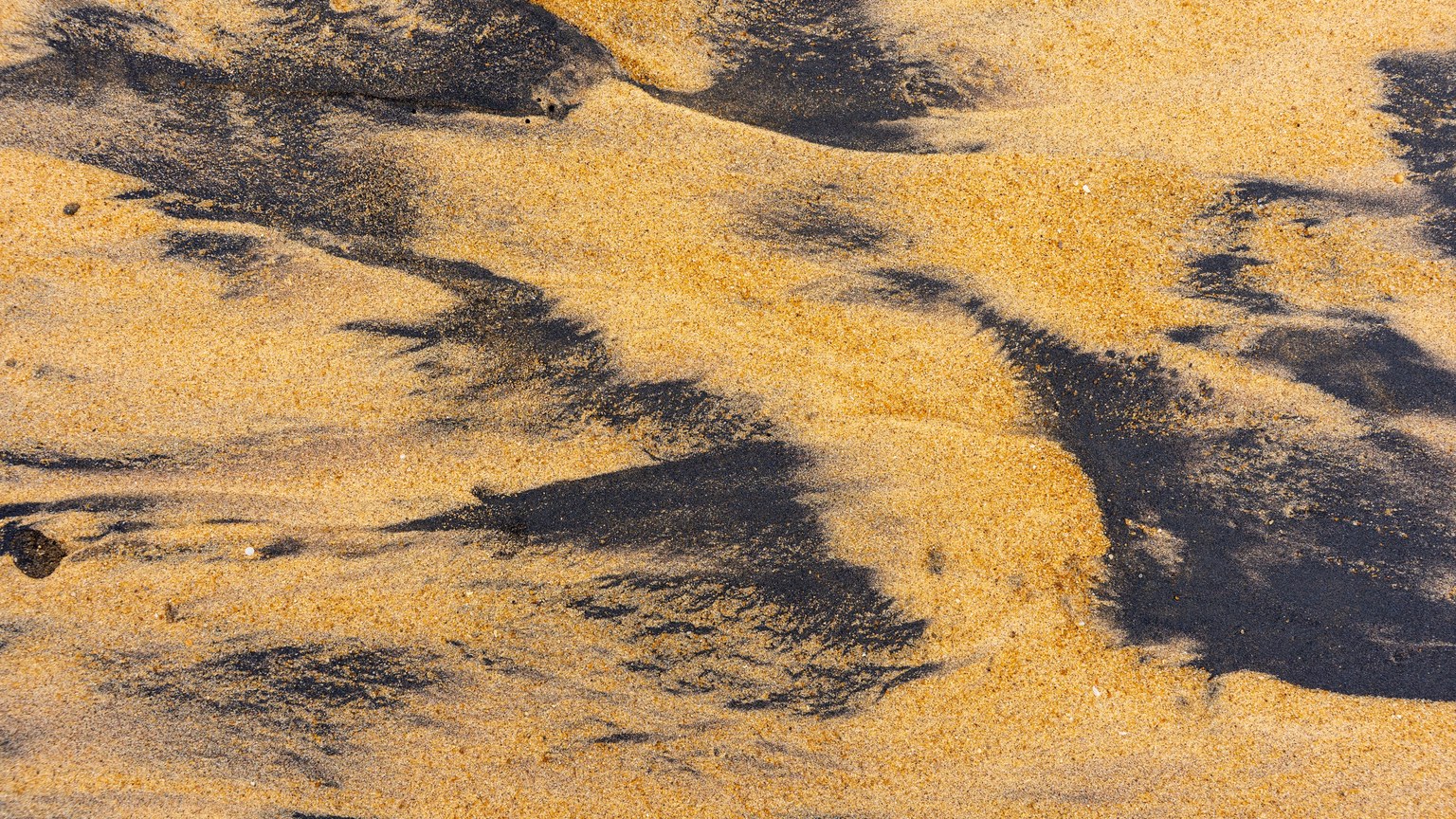Detailed close-up of sand textures with ilmenite on a beach, highlighting natural patterns.