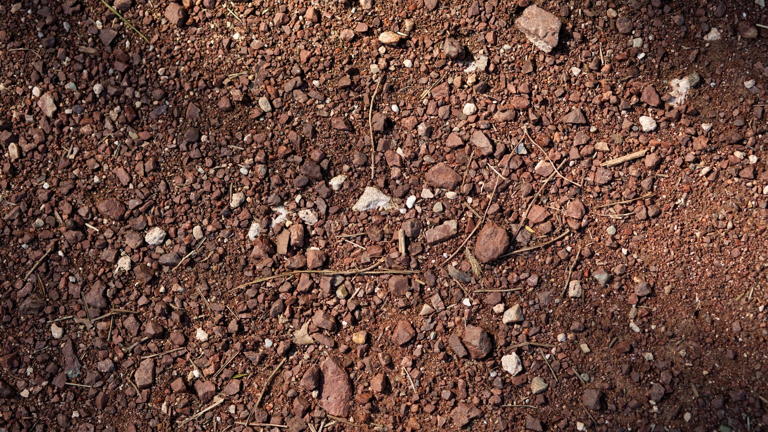 Detailed texture of red rocky soil with natural shadows, showcasing earth patterns.