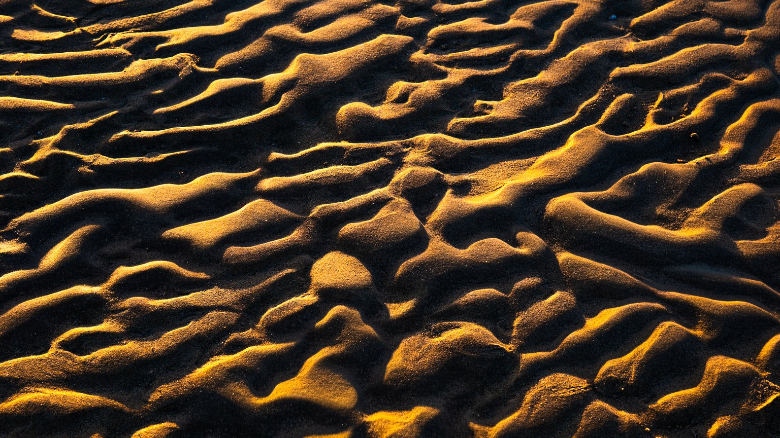 Capture of sunlit sand patterns creating a striking abstract texture on a Kuwaiti beach.