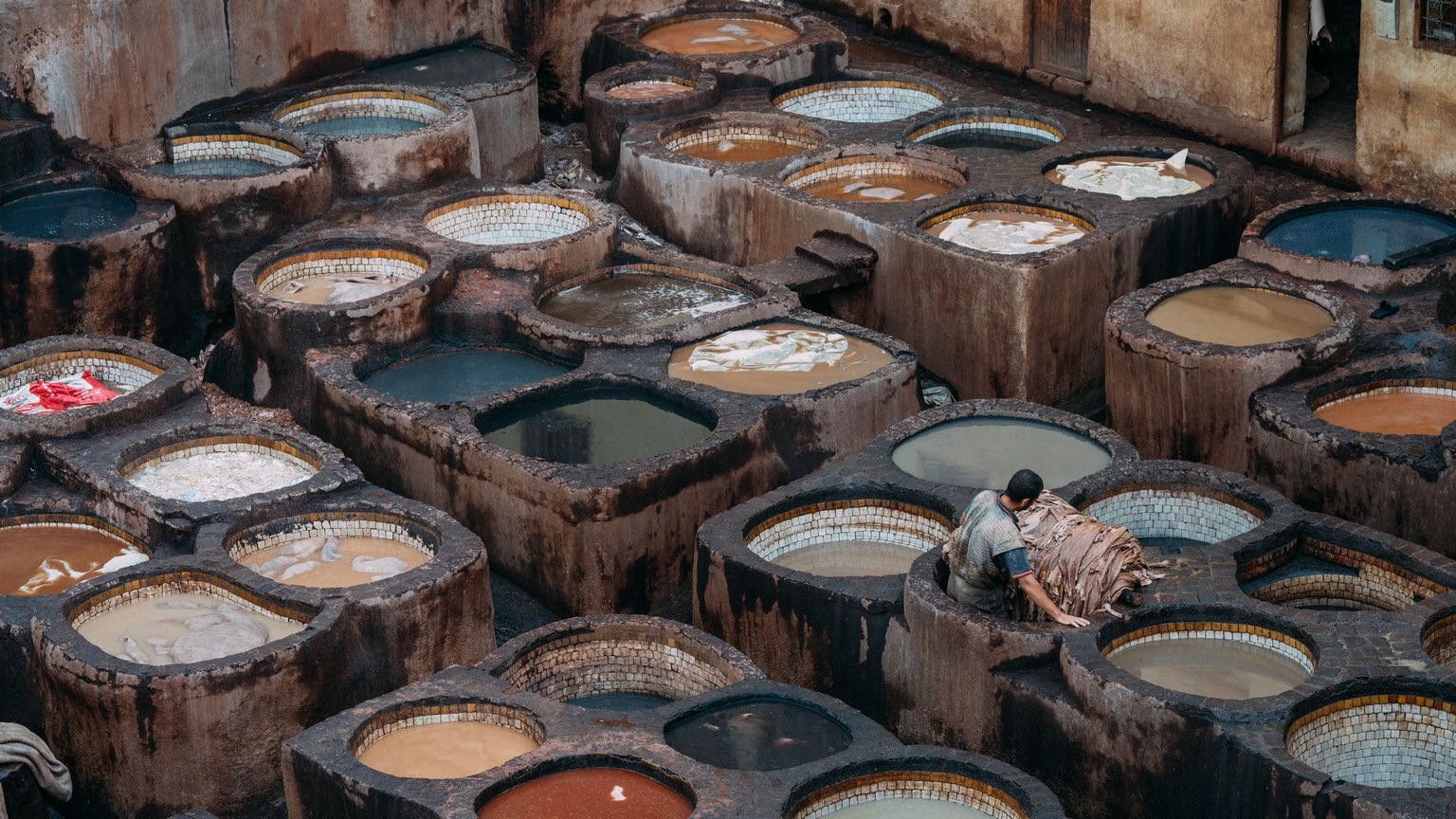 A man works at a traditional leather tannery in Fes, showcasing numerous dye pits.