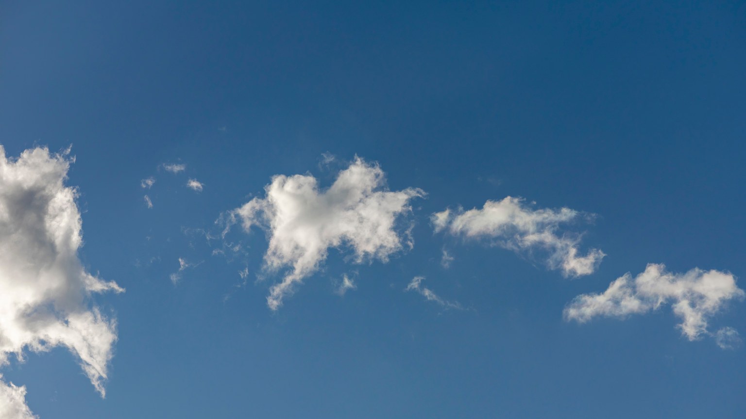 A clear blue sky featuring fluffy white clouds bathed in sunlight.